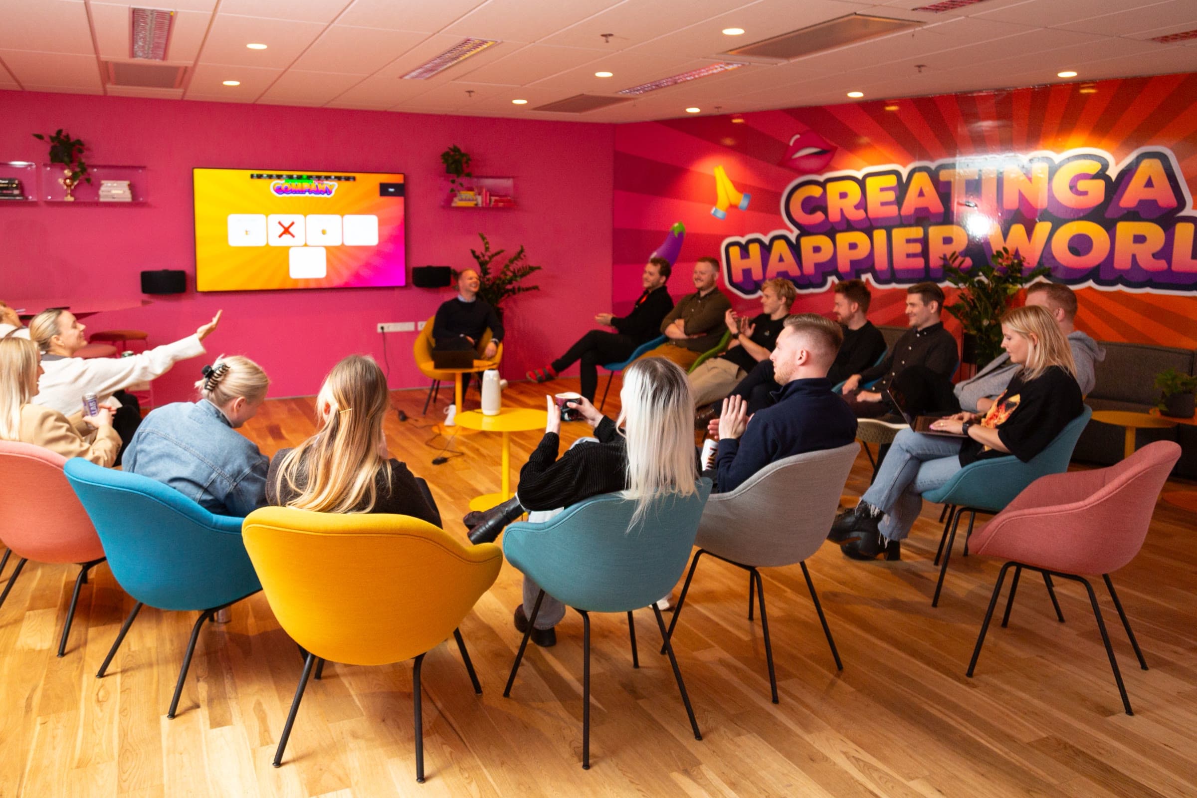 The team in a ring of coloured armchairs, watching a game on the big screen